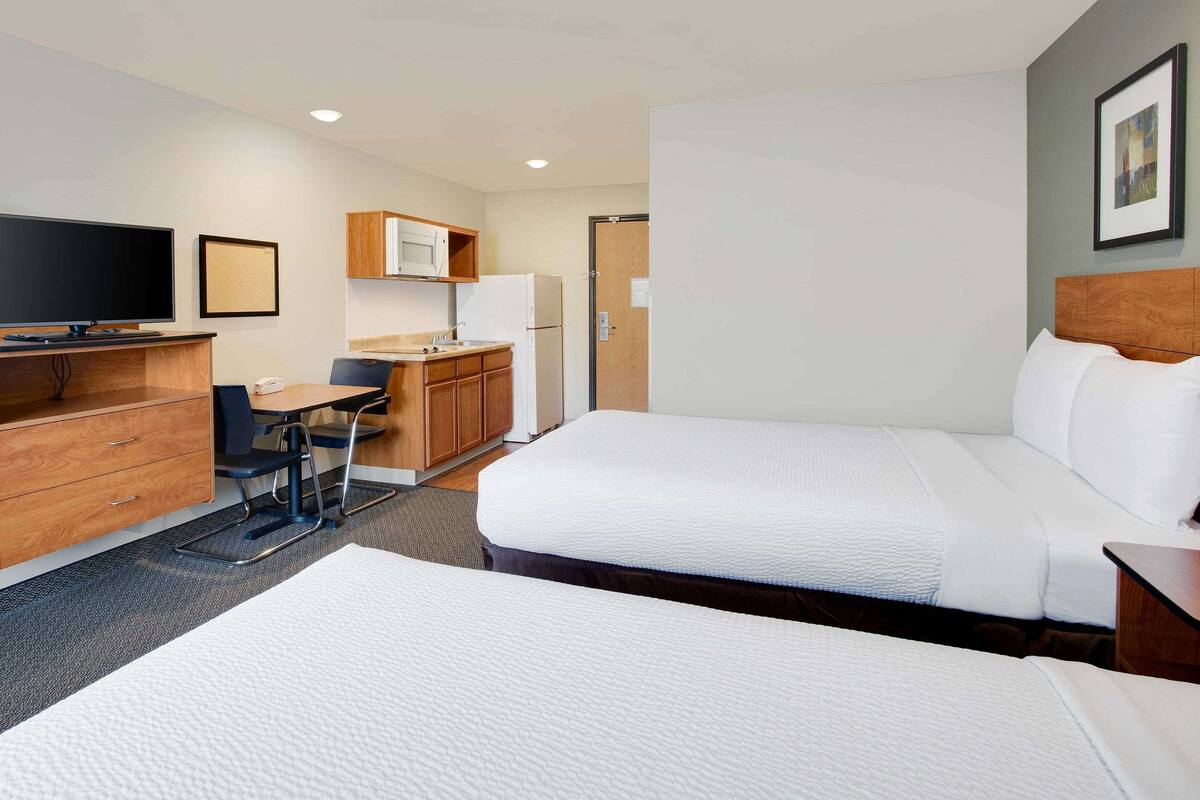 A hotel room with two beds, a desk, a chair, a microwave, and a refrigerator.