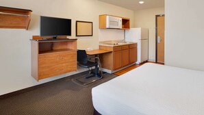 A compact hotel room with a bed, a desk with a chair, a television, a microwave, and a refrigerator.