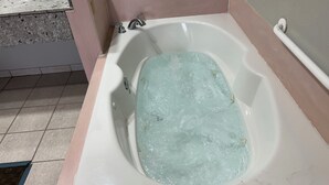 A bathtub with running water, a tiled floor, and a corner wall with a pink trim. - Howards Inn Motel (Eunice)