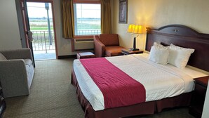 A hotel room with a large bed, a chair, a desk, and a view of the outdoors. - Howards Inn Motel (Eunice)