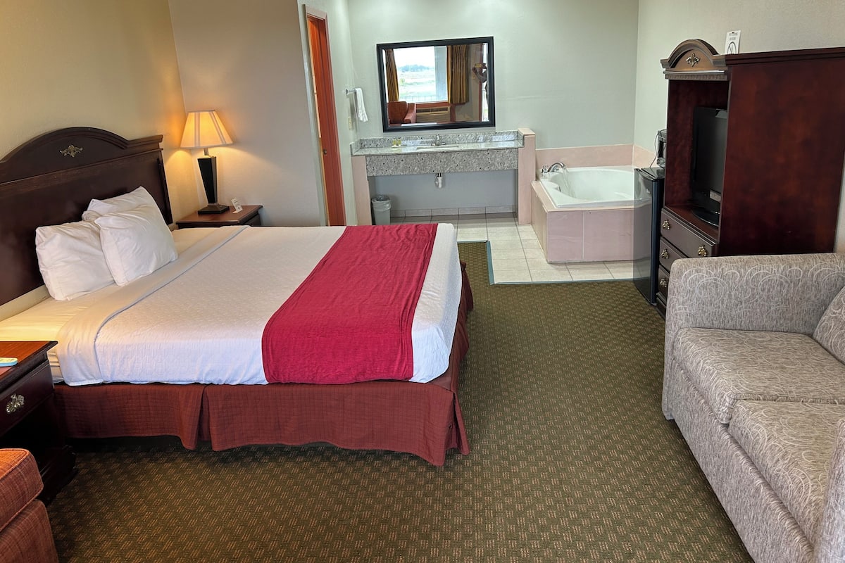 A hotel room with a bed, a sofa, a bathroom with a bathtub, a TV, and a mirror.