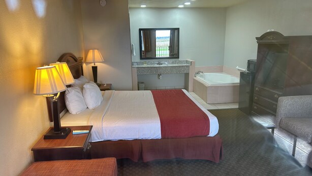 A hotel room with a bed, two bedside lamps, a nightstand, a dresser, a mirror, a bathroom with a sink and bathtub, and a small seating area. - Howards Inn Motel (Eunice)