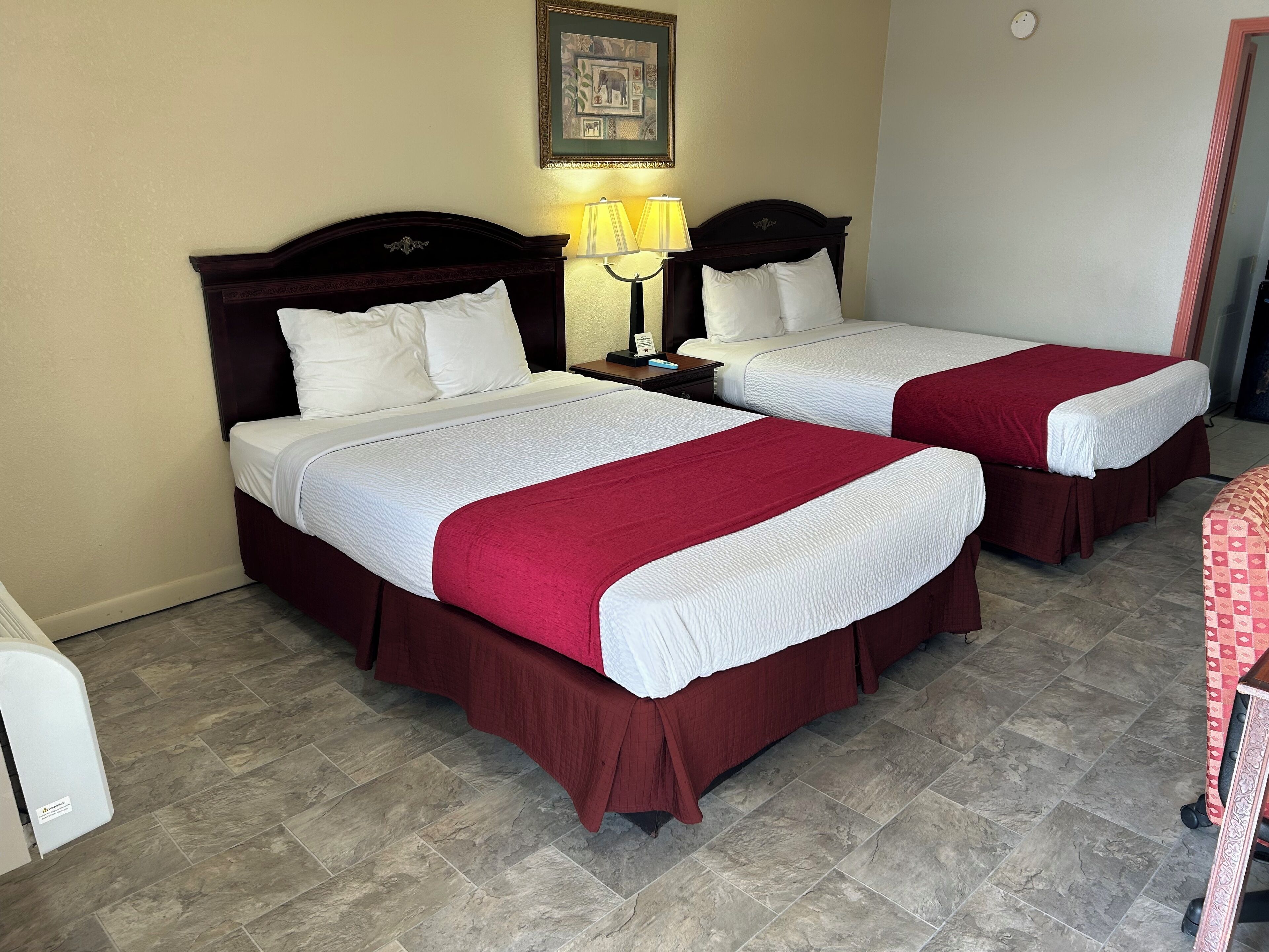Two single beds with red and white bedding, a nightstand with a lamp, and a framed picture on the wall.