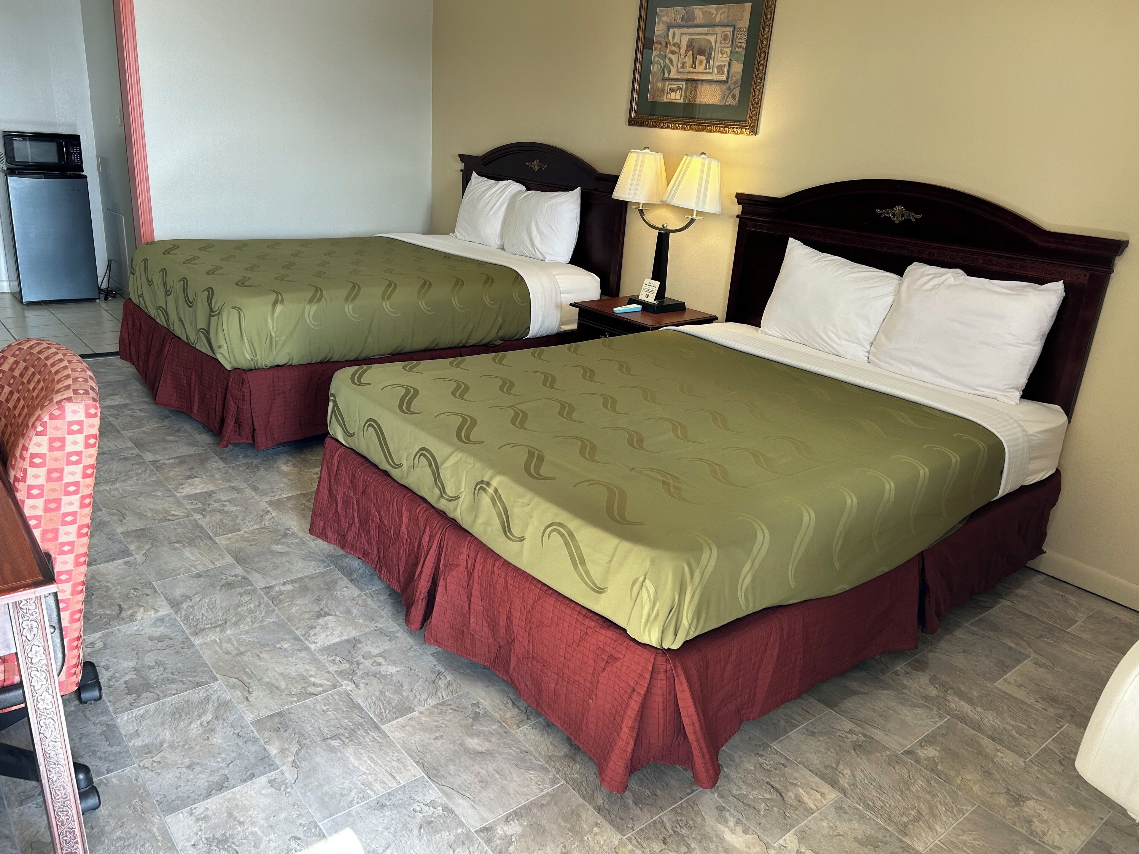 Camera d'albergo con due letti, ognuno con lenzuola verdi e rosse, un comodino con una lampada e un quadro appeso al muro.