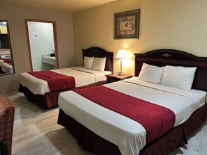 A hotel room with two beds, each with a red and white bedspread, a nightstand with a lamp, a framed picture on the wall, and a mirror on the left.