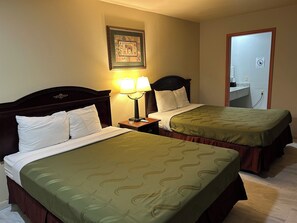 A hotel room with two single beds, a nightstand with a lamp, a framed picture on the wall, and a door with a 'No Smoking' sign.