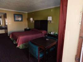 Habitación de hotel con dos camas, un escritorio, una silla, una mesita de noche, una lámpara y un cuadro en la pared.