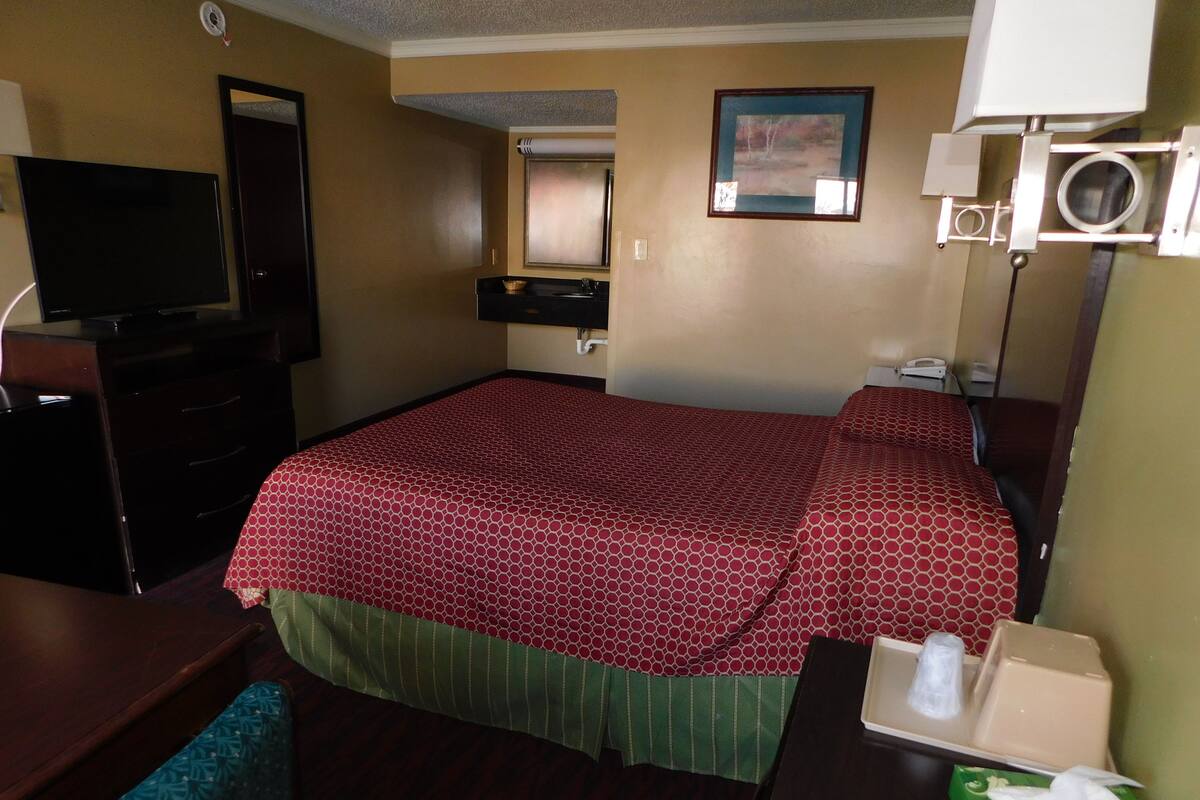 Une chambre d’hôtel avec un grand lit, une télévision, un bureau avec un téléphone et un miroir.