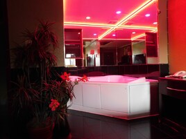 Un baño moderno con un espejo grande, una bañera blanca y detalles de iluminación roja.
