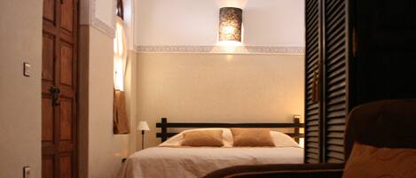 Una habitación tenuemente iluminada con una cama, una mesa con una vela y un frutero.