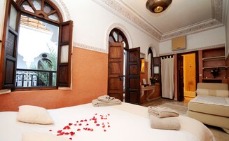 Habitación de hotel con una cama grande, un área de descanso con sofá, una mesita con un florero y vistas al exterior a través de una ventana.