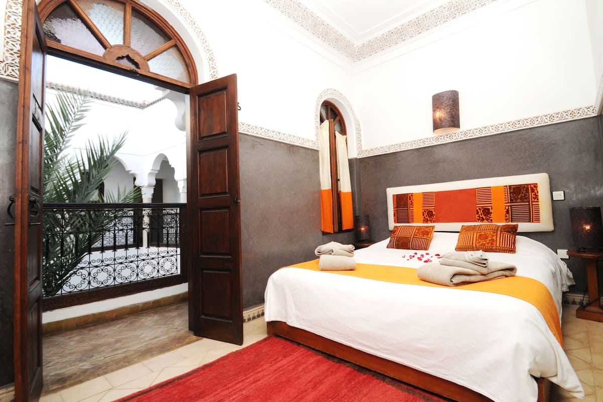 Habitación de hotel con cama, un espejo grande, una alfombra roja y vistas a un patio.