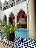 Un área de piscina con suelo a cuadros, plantas en macetas y una fuente decorativa.
