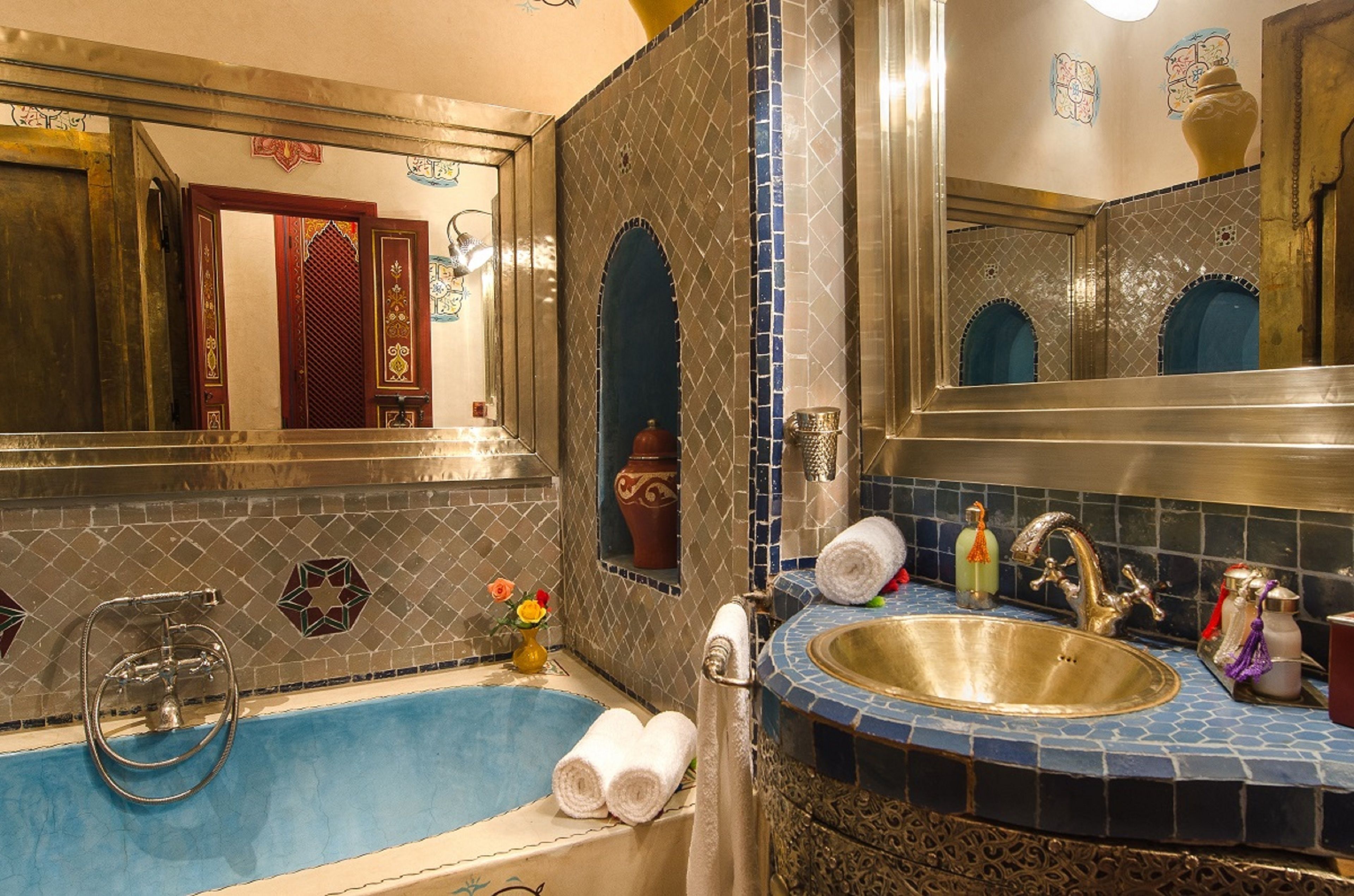 A bathroom with a blue-tiled sink, a bathtub, and a large mirror.