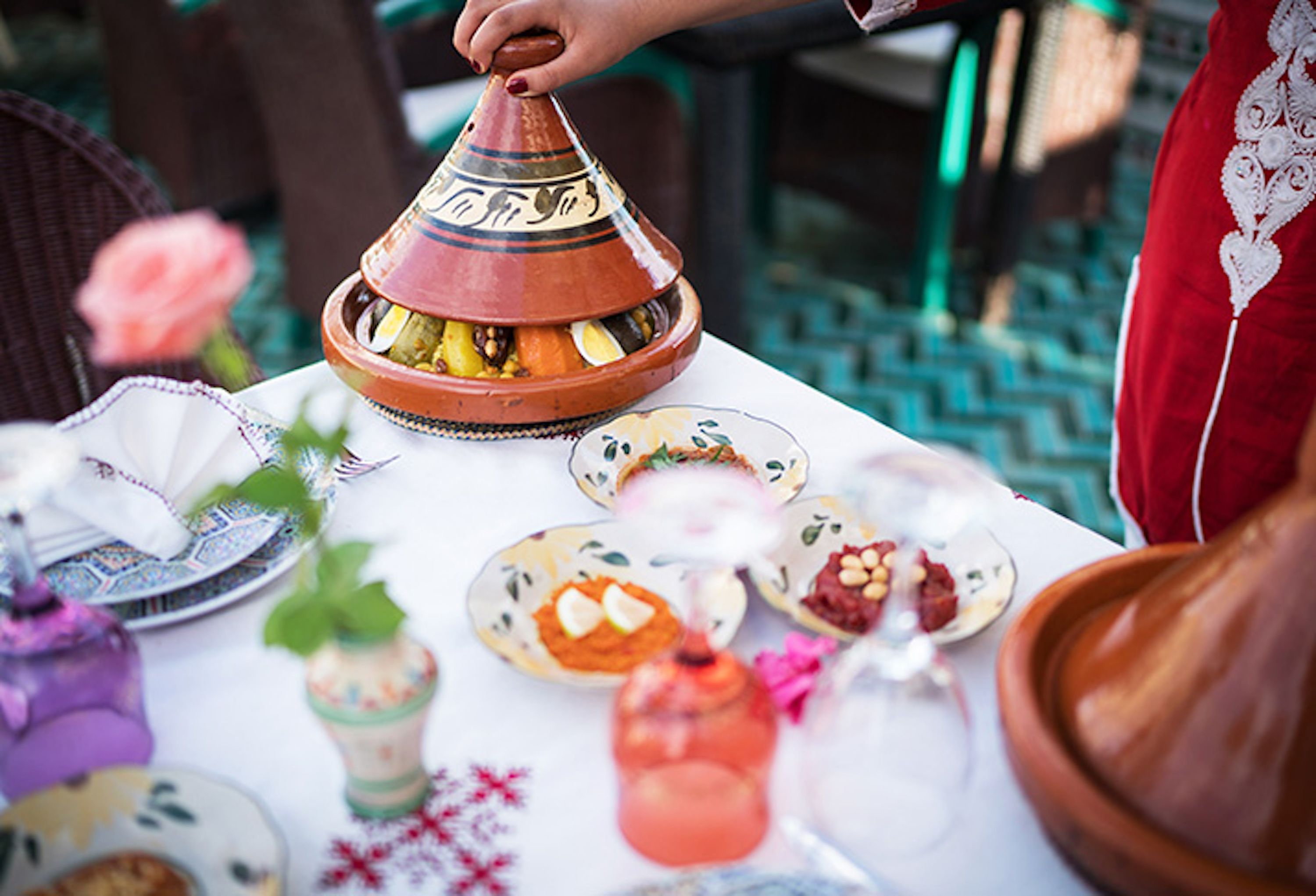 A table set with various dishes, including a tagine, plates, and a drink.