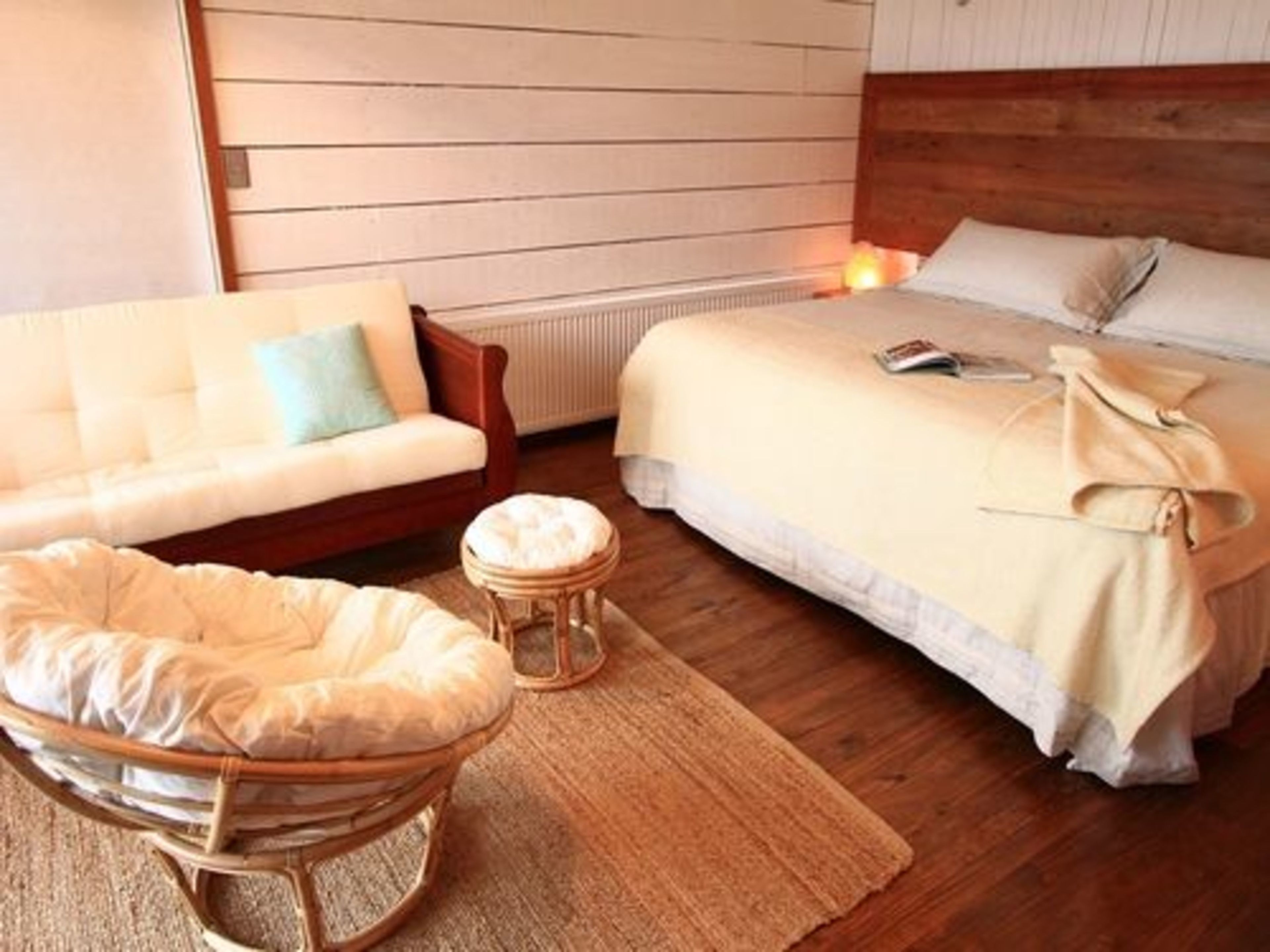 Un dormitorio acogedor con cama, cabecera de madera, sofá blanco y una silla de mimbre.