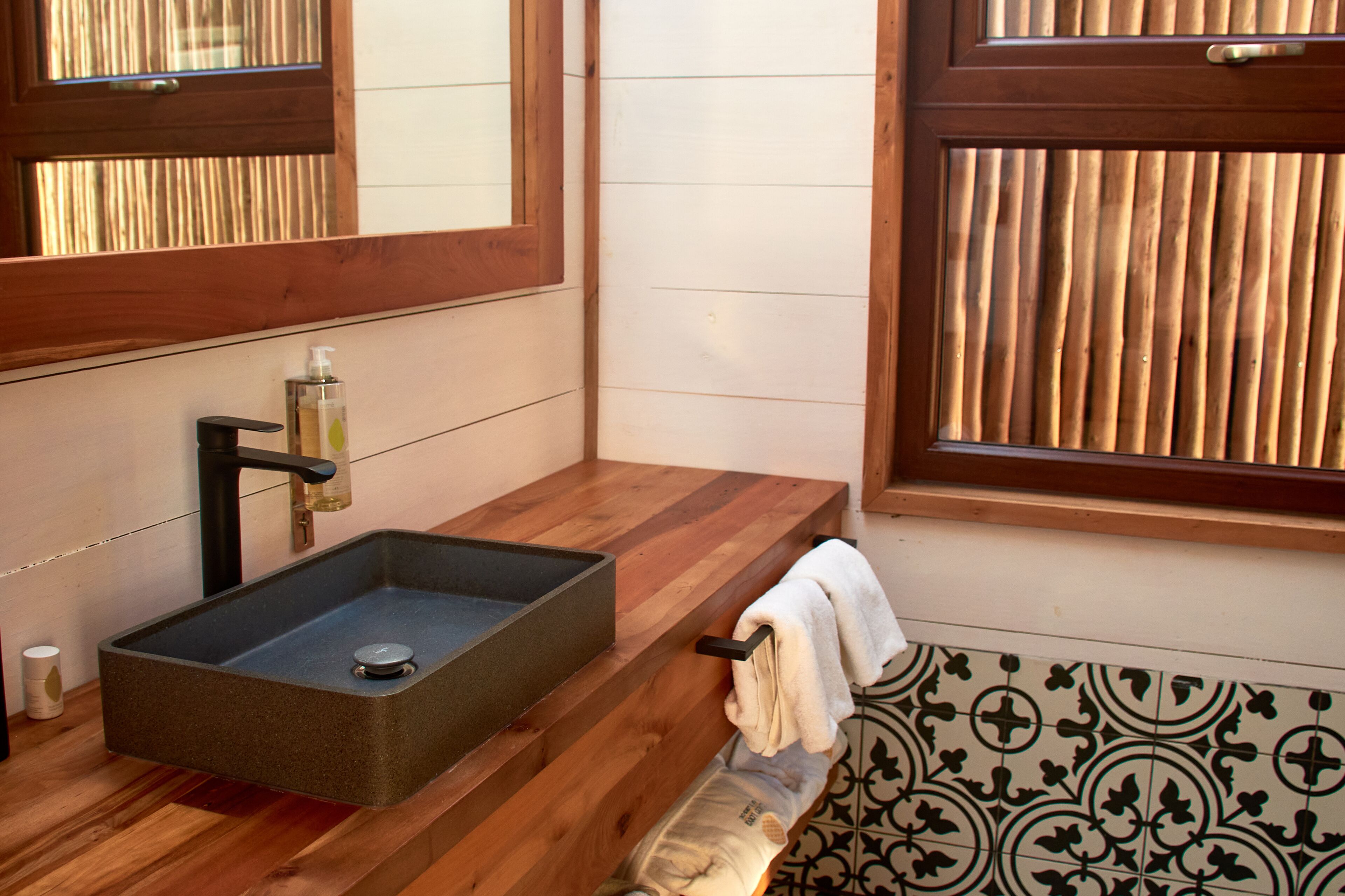 Un baño con tocador de madera, un lavamanos rectangular y una toalla colgada en la pared.
