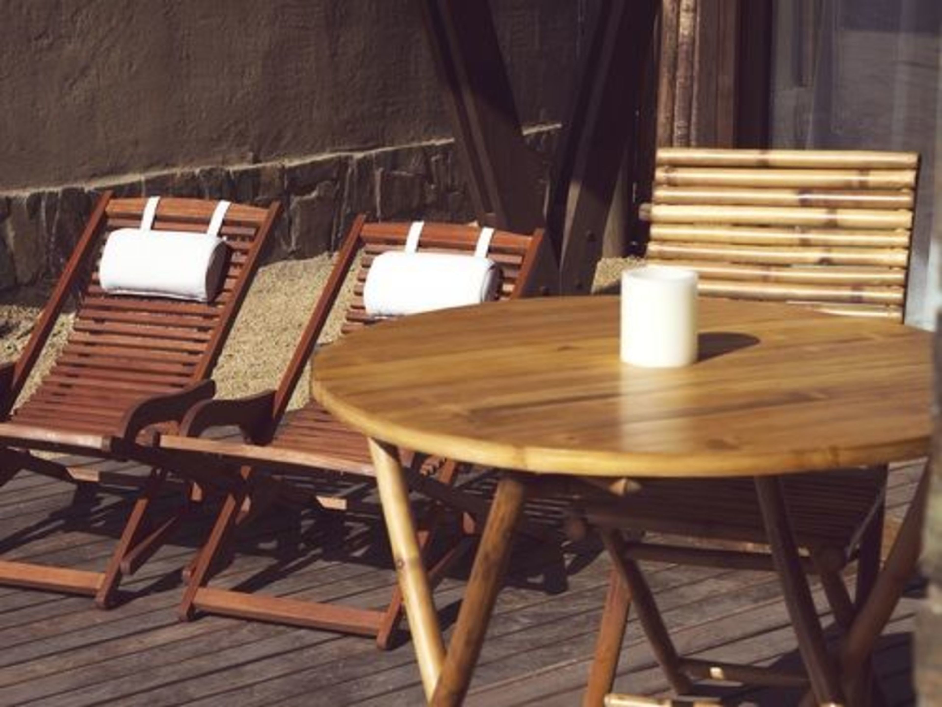 Una terraza de madera con dos sillones de descanso y una mesa redonda, una con una vela blanca.