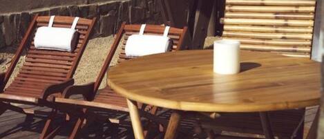 Una terraza de madera con dos sillones de descanso y una mesa redonda, una con una vela blanca.