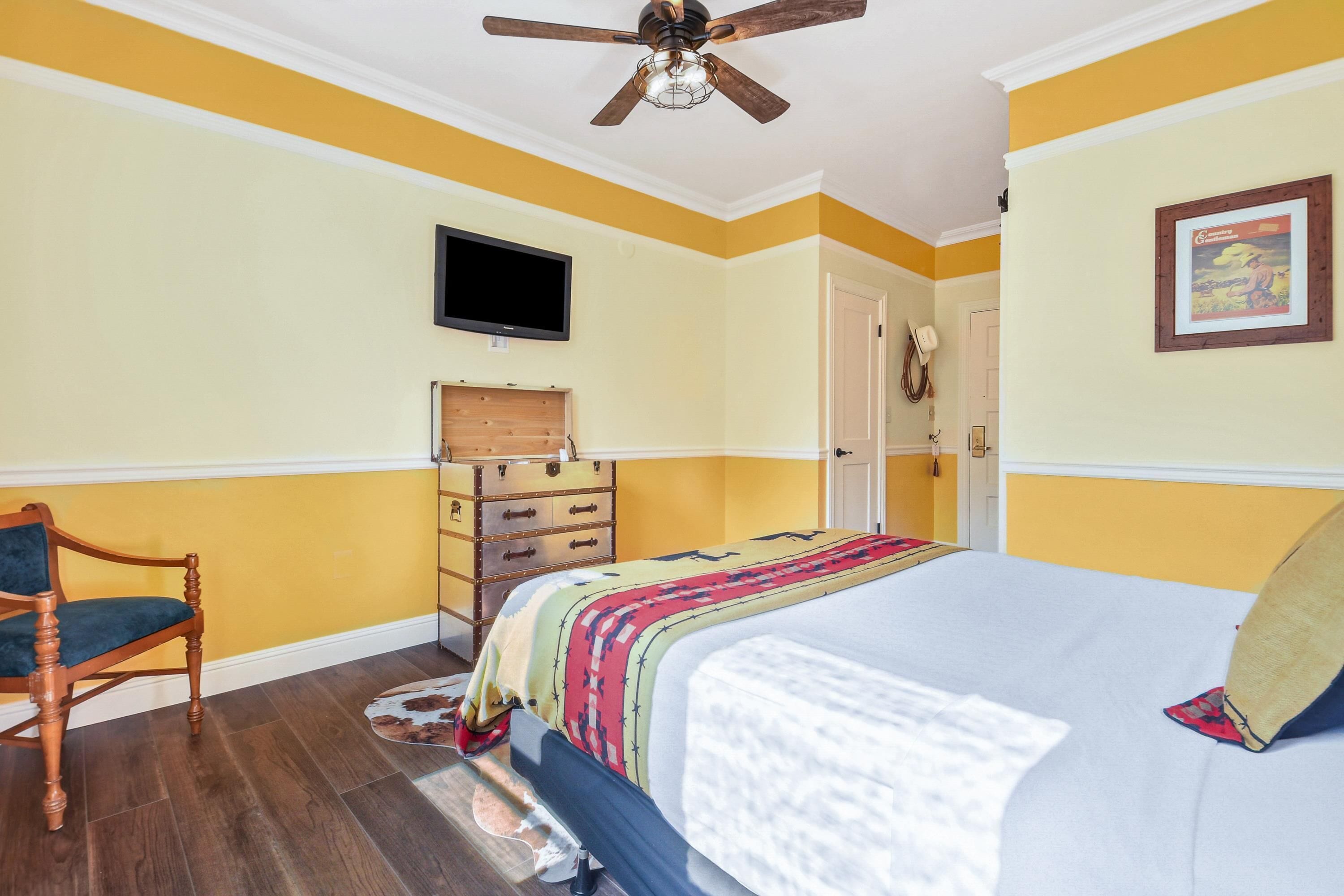A bedroom with a bed, wooden dresser, television, and a ceiling fan.