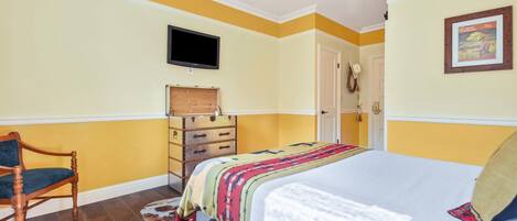 A bedroom with a bed, wooden dresser, television, and a ceiling fan.