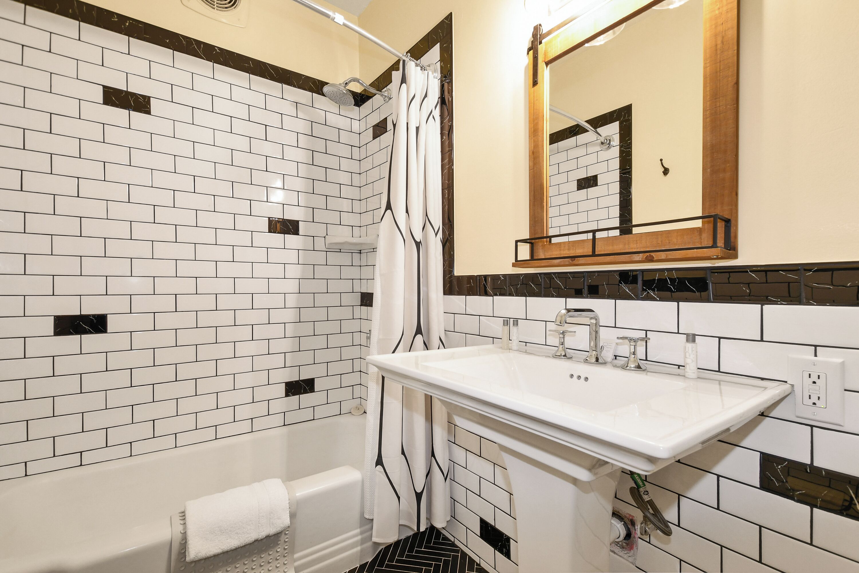 A bathroom with white and black tiled walls, a white sink, and a shower with a white curtain.