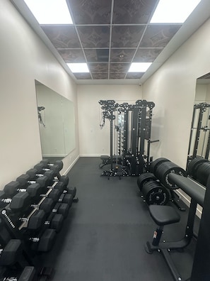 Un gimnasio con equipamiento de levantamiento de pesas, espejos y una banca.