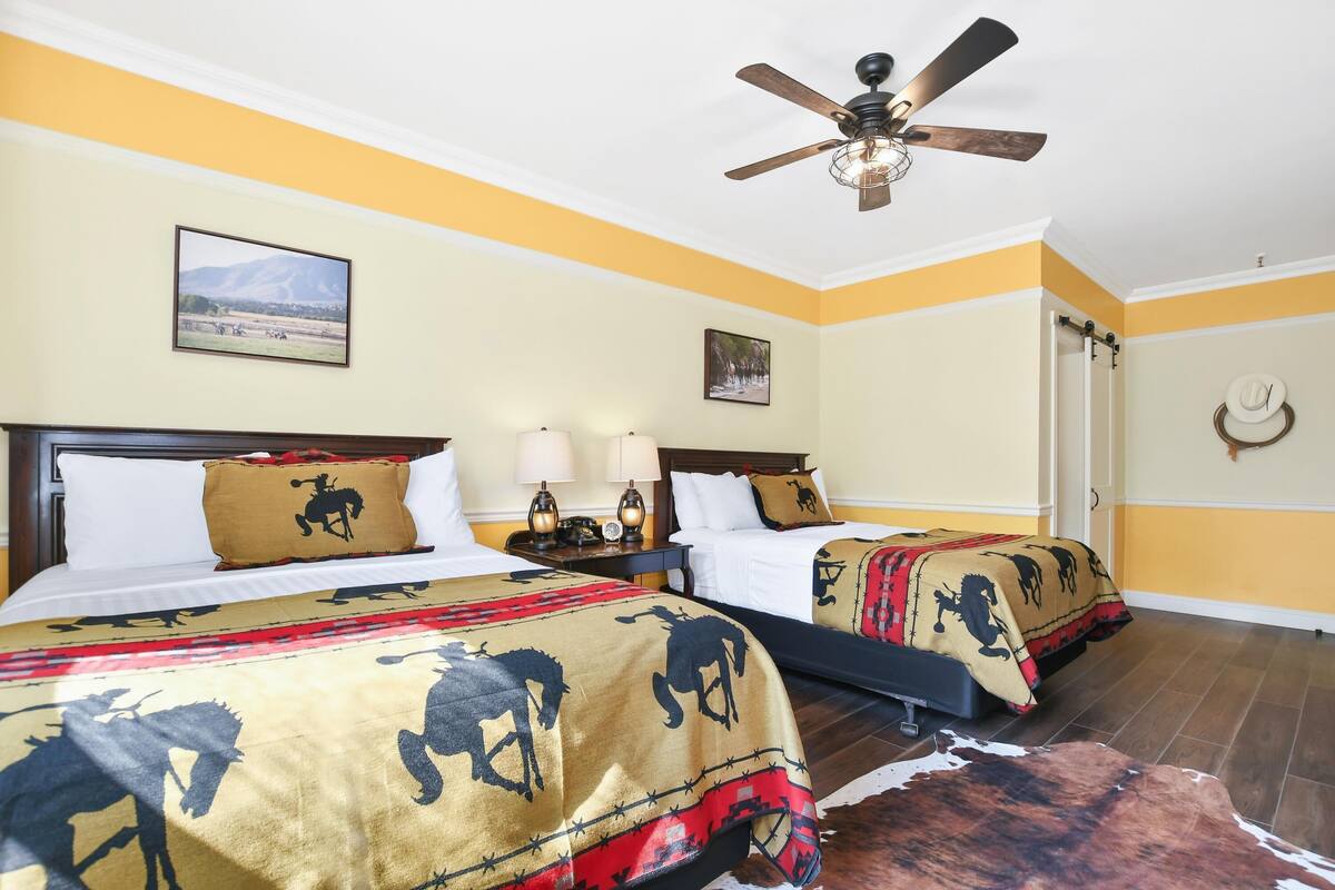Habitación de hotel con dos camas, cada una con un diseño de manta diferente, un ventilador de techo y un cuadro en la pared.