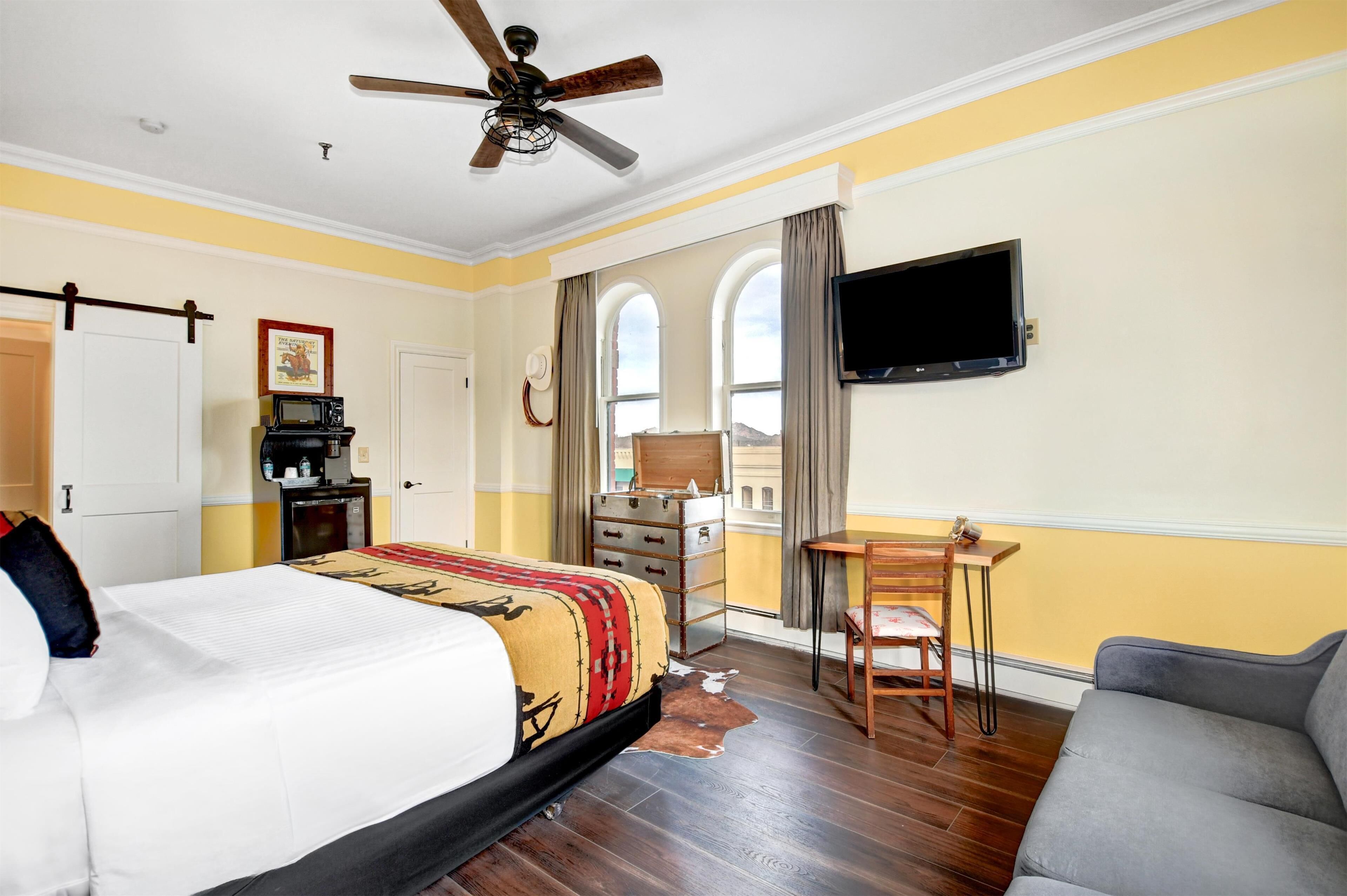 A hotel room with a bed, a desk, a TV, and a view of the outside.