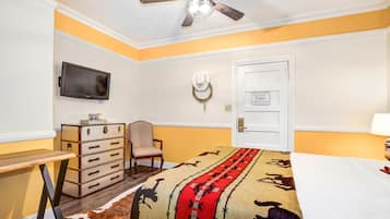 A hotel room with a bed, a desk, a chair, a television, a door, and a ceiling fan.