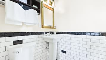 A bathroom with a white pedestal sink, a white bathtub, black and white tiled walls, and a mirror with three lights.