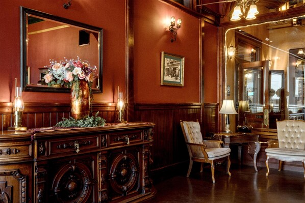 Una habitación ricamente decorada con un espejo grande, una consola de madera con un jarrón de flores y dos sillones tapizados.