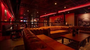 A dimly lit lounge area with leather seating and tables, featuring a brick wall and red lighting accents. - Hotel St. Michael, BW Premier Collection (Prescott)