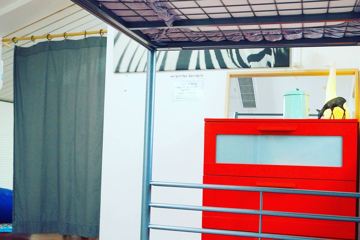 A room with a bed, a red cabinet, a curtain, and a bulletin board.