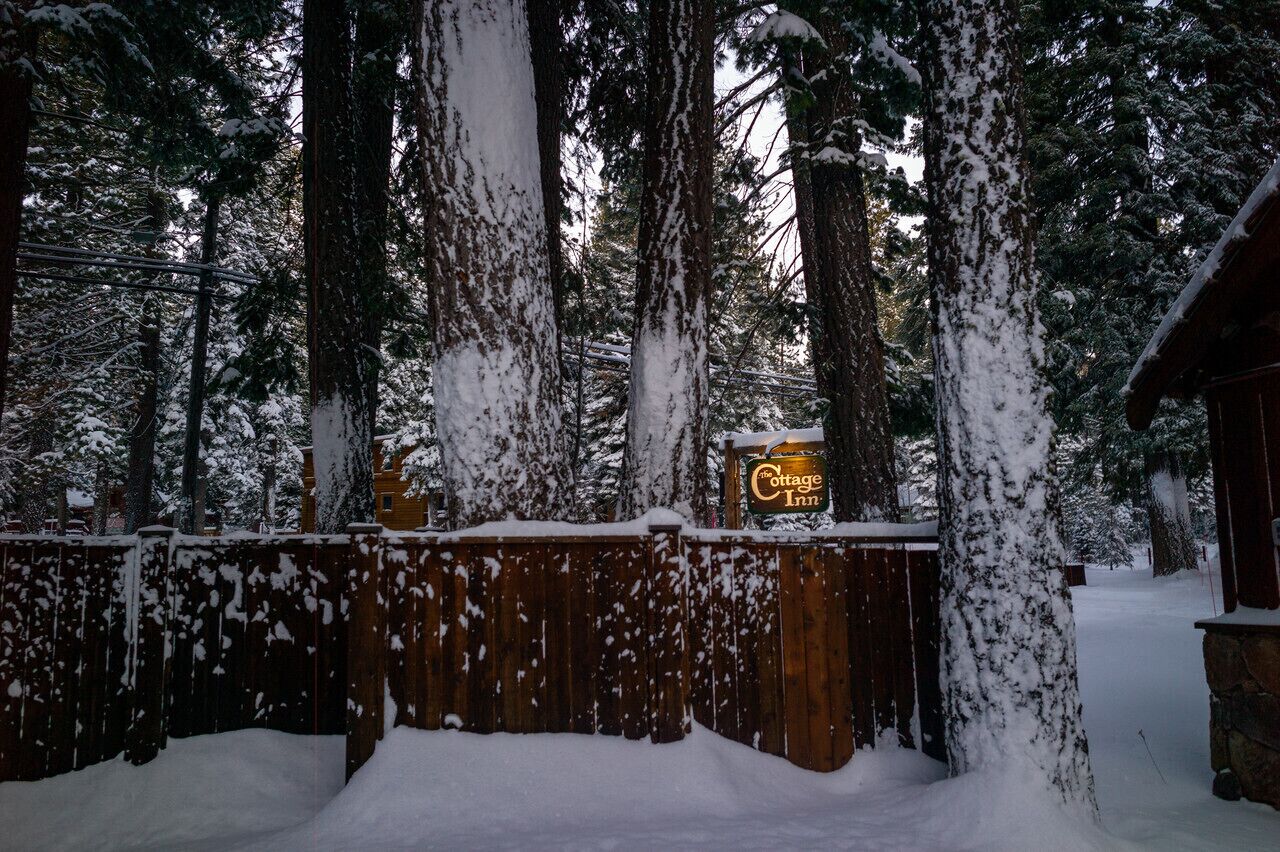 Une clôture en bois recouverte de neige, avec une enseigne indiquant « The Cottage Inn » en arrière-plan.