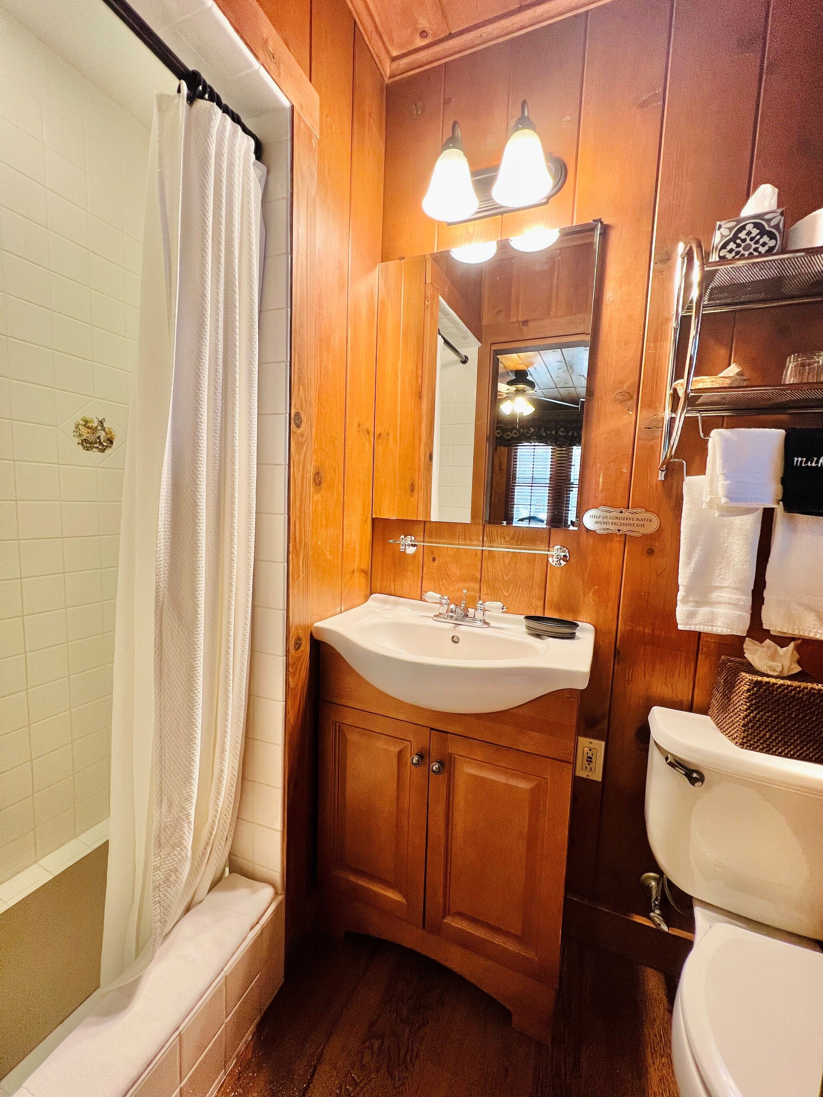 Un baño de madera con un lavamanos, espejo y retrete blancos.