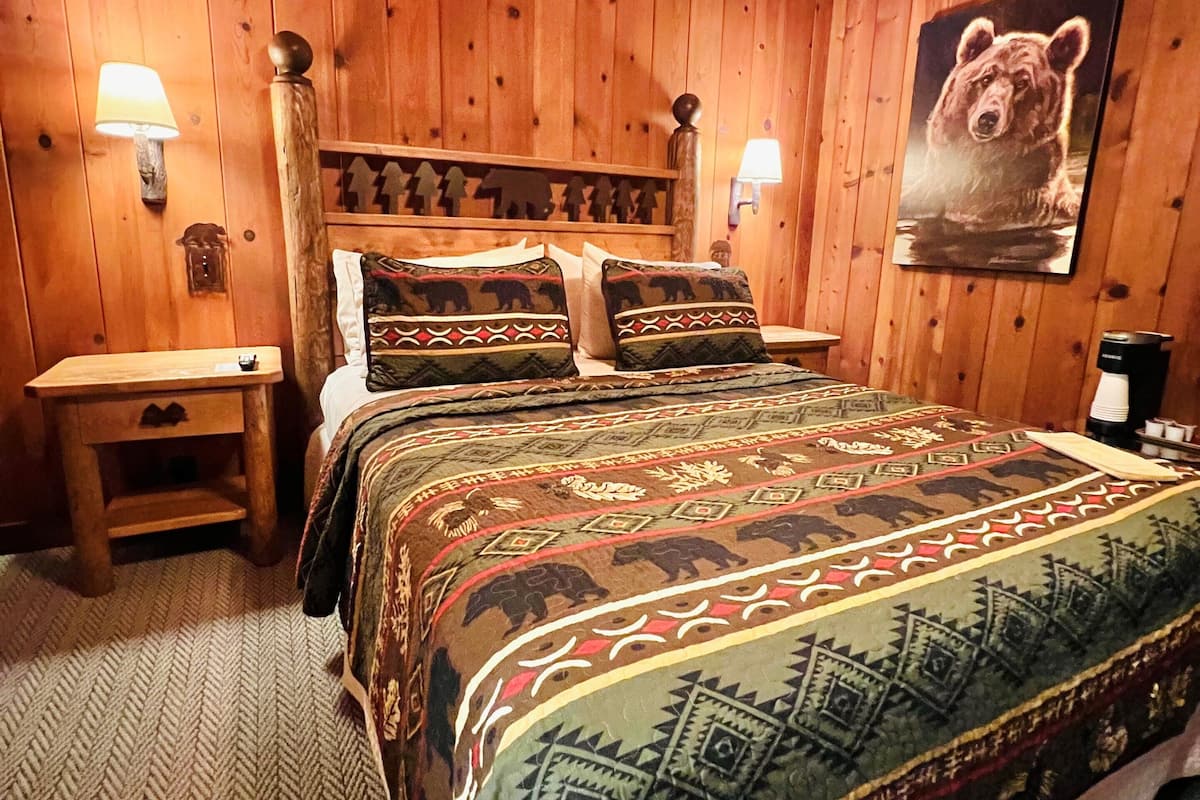 Habitació amb panells de fusta, un llit, dues taules de nit i una làmpada penjada a la paret.