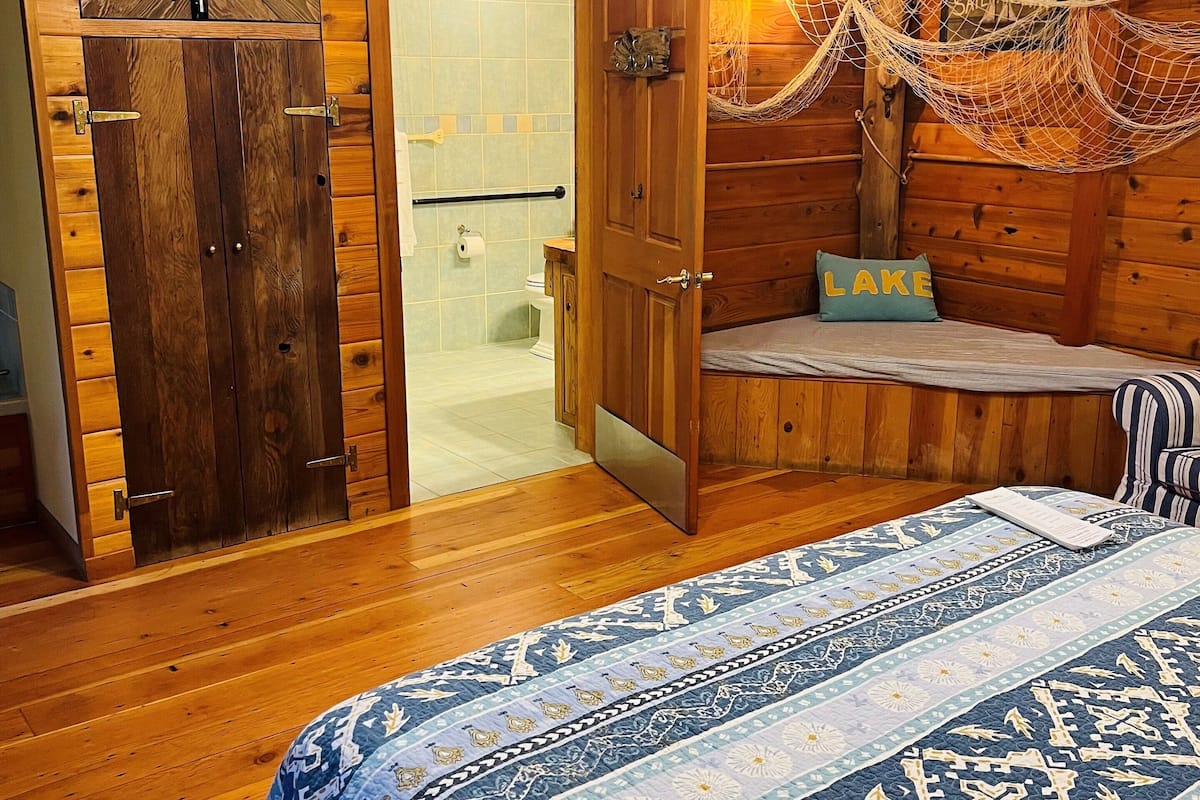 Habitació d'una cabana de fusta amb un llit, una cadira d'hamaca i una televisió.