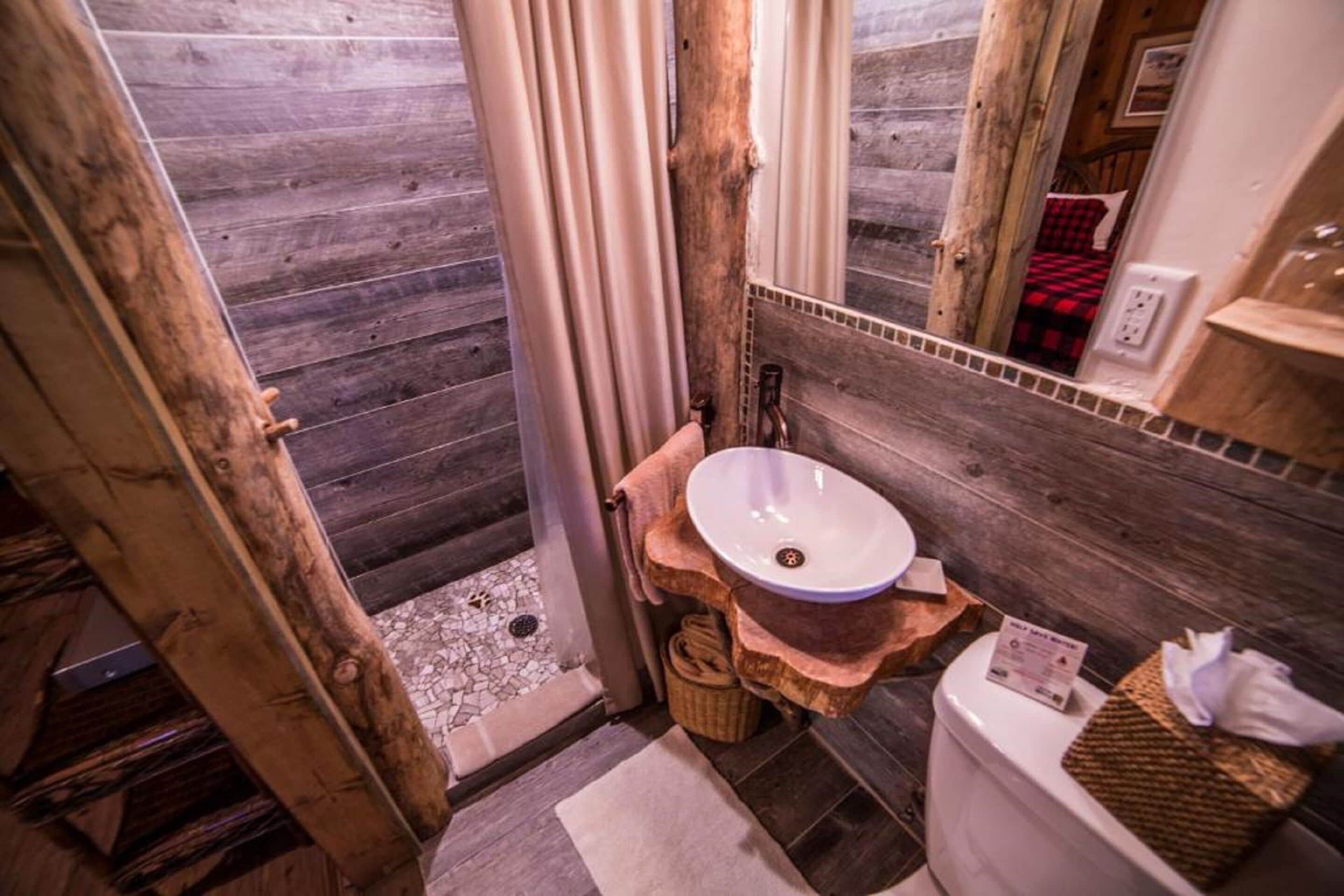Une salle de bain rustique avec un plancher en bois, un lavabo rond et un miroir.