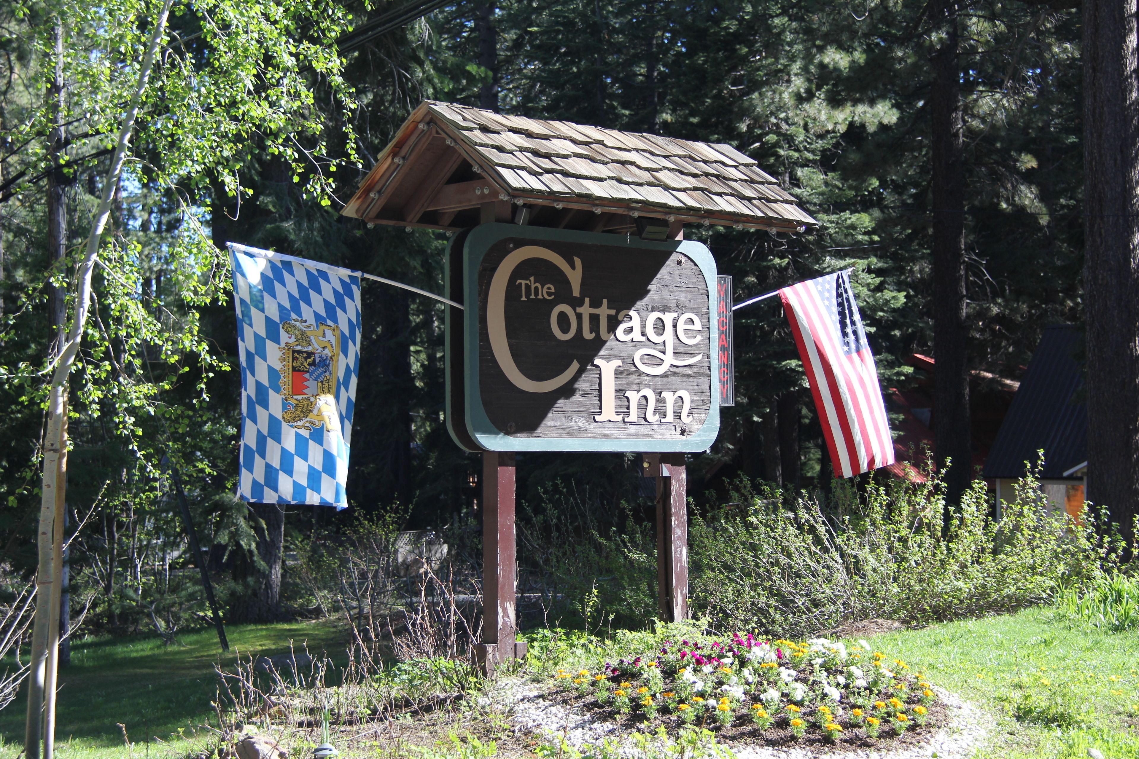 Een bordje voor The Cottage Inn, met een rustieke houten constructie, omringd door groen en bloemen.
