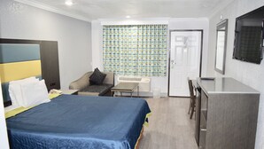 A hotel room with a large bed, a desk, a chair, a small table, a mirror, and a door. - Budget Inn La Puente (La Puente)