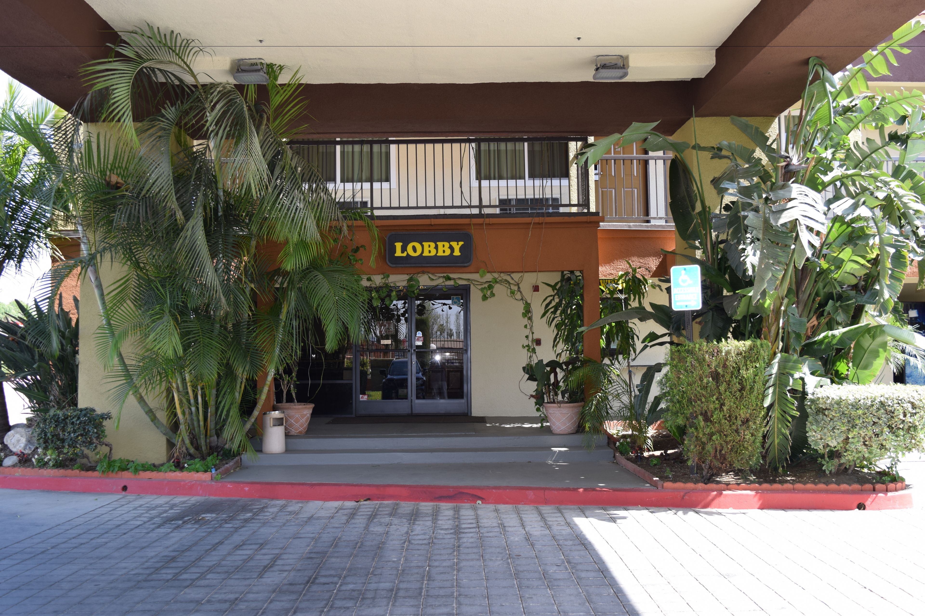 A hotel lobby with a 'Lobby' sign, potted plants, and a red curb.