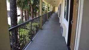 A long corridor with a balcony on one side, palm trees, and a door with the number 220. - Budget Inn La Puente (La Puente)