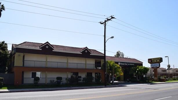 A two-story motel with a red-tiled roof, a balcony on the second floor, and a signboard advertising the Budget Inn. - Budget Inn La Puente (La Puente)