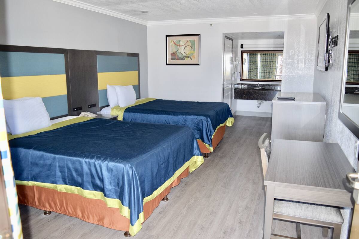 A hotel room with two beds, a small kitchenette, a dining table, and a bathroom visible through an open door.