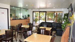 A restaurant interior with wooden tables and chairs, a black leather sofa, and a counter with a plant. - Budget Inn La Puente (La Puente)