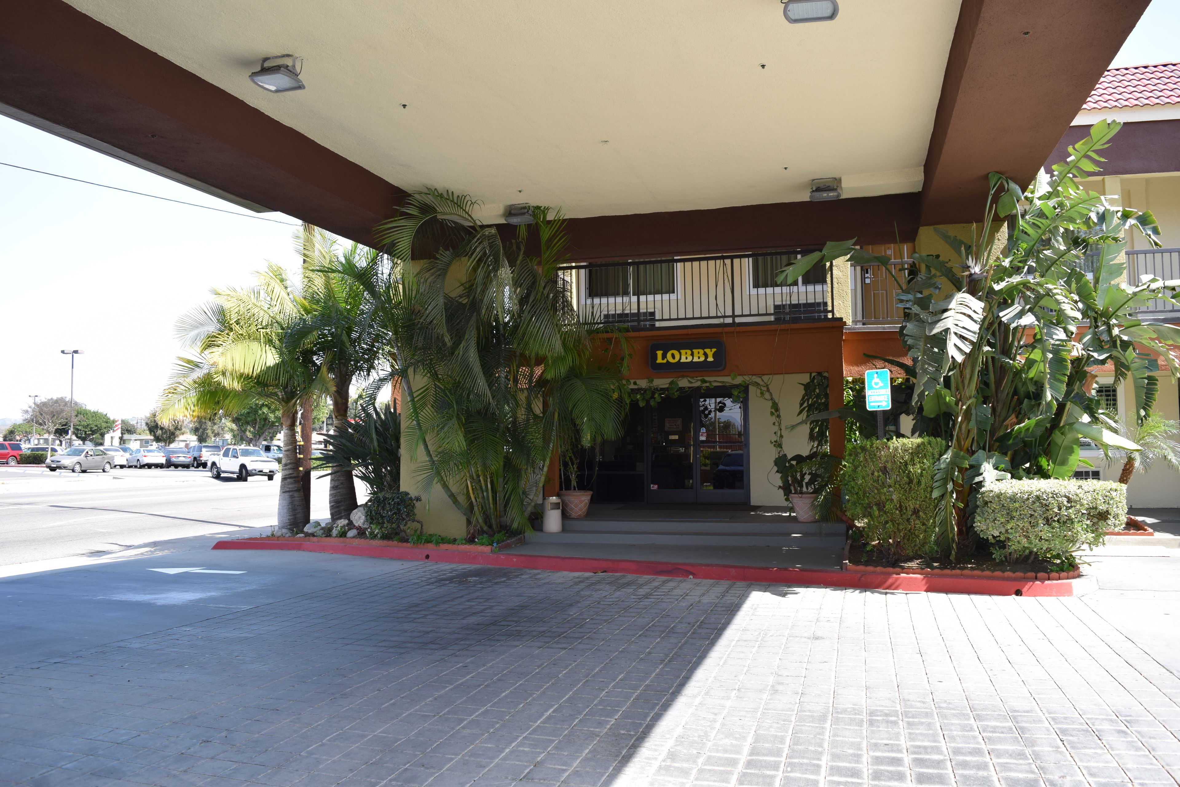 Un edificio con un letrero que dice 'Lobby', una bordeadora roja y un acceso pavimentado con plantas en macetas.