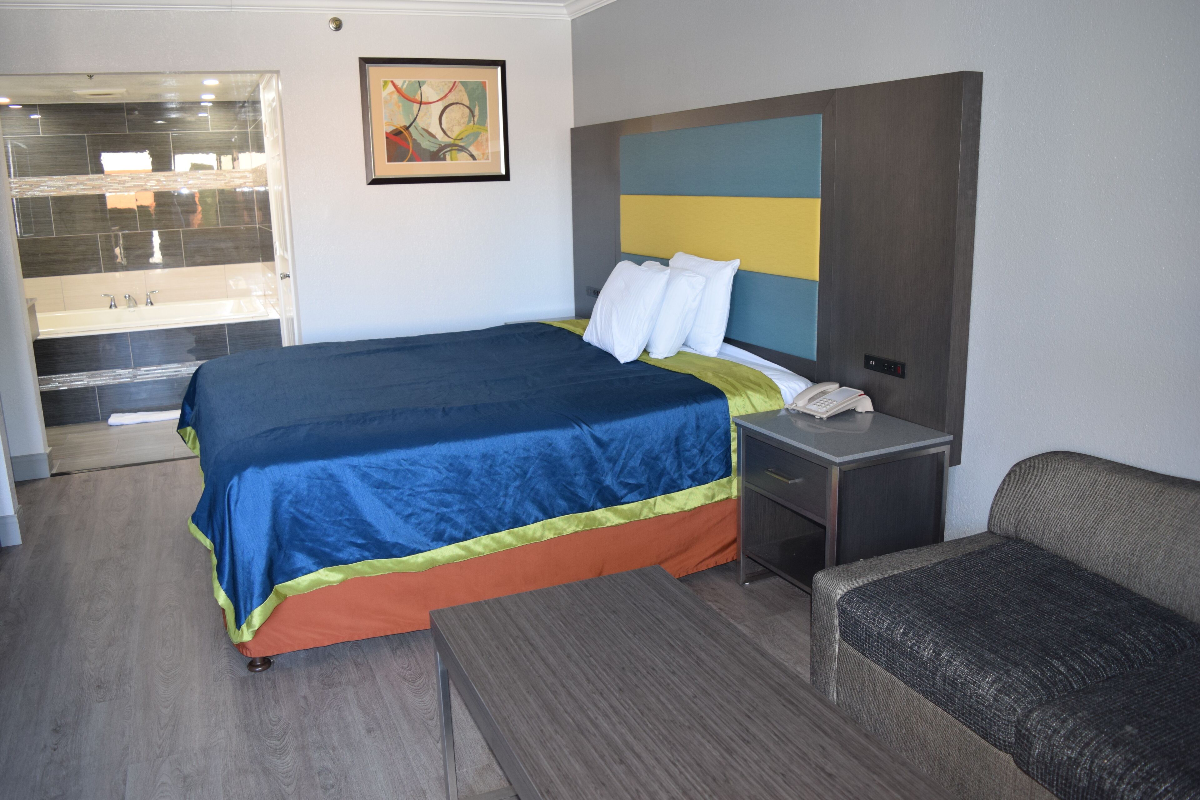 A hotel room with a bed, a bedside table, a chair, and a bathroom visible through an open door.