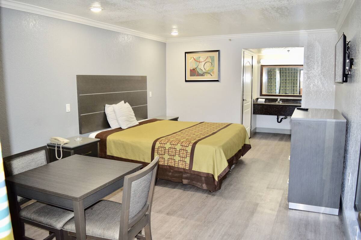 A hotel room with a bed, a desk, a chair, a telephone, a mirror, and a sink.