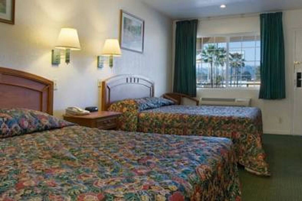 Een hotelkamer met twee bedden, een bureau, een stoel, een raam met gordijnen en een deur.